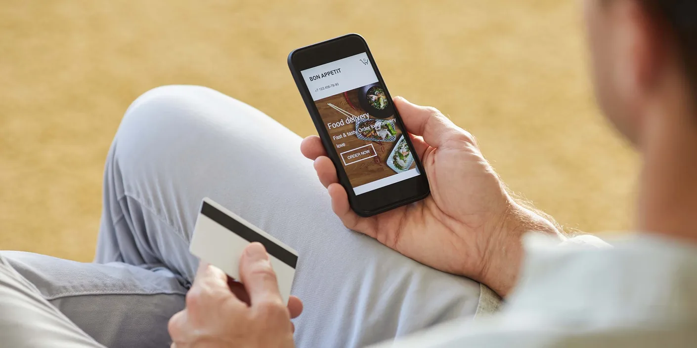 Close-up of young man using mobile phone to order food delivery he paying with credit card