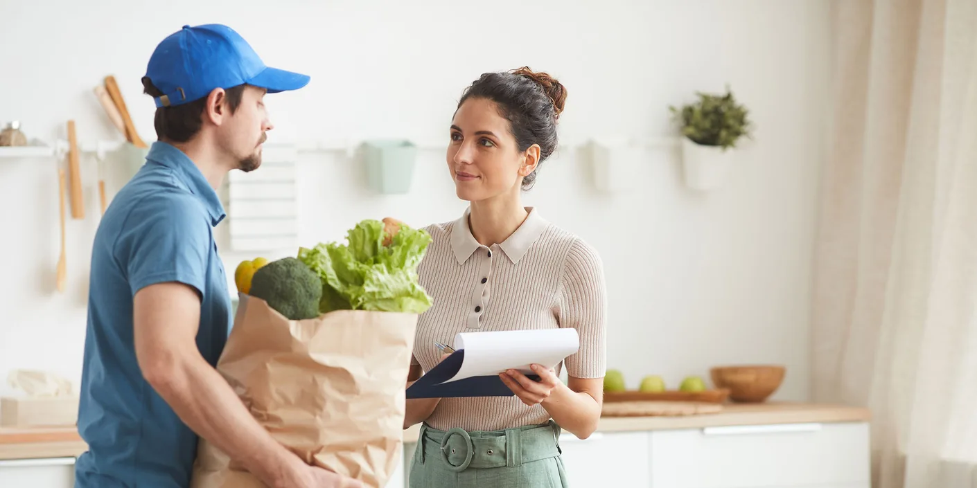 Delivery man in uniform delivering the food to woman while she signing for delivery